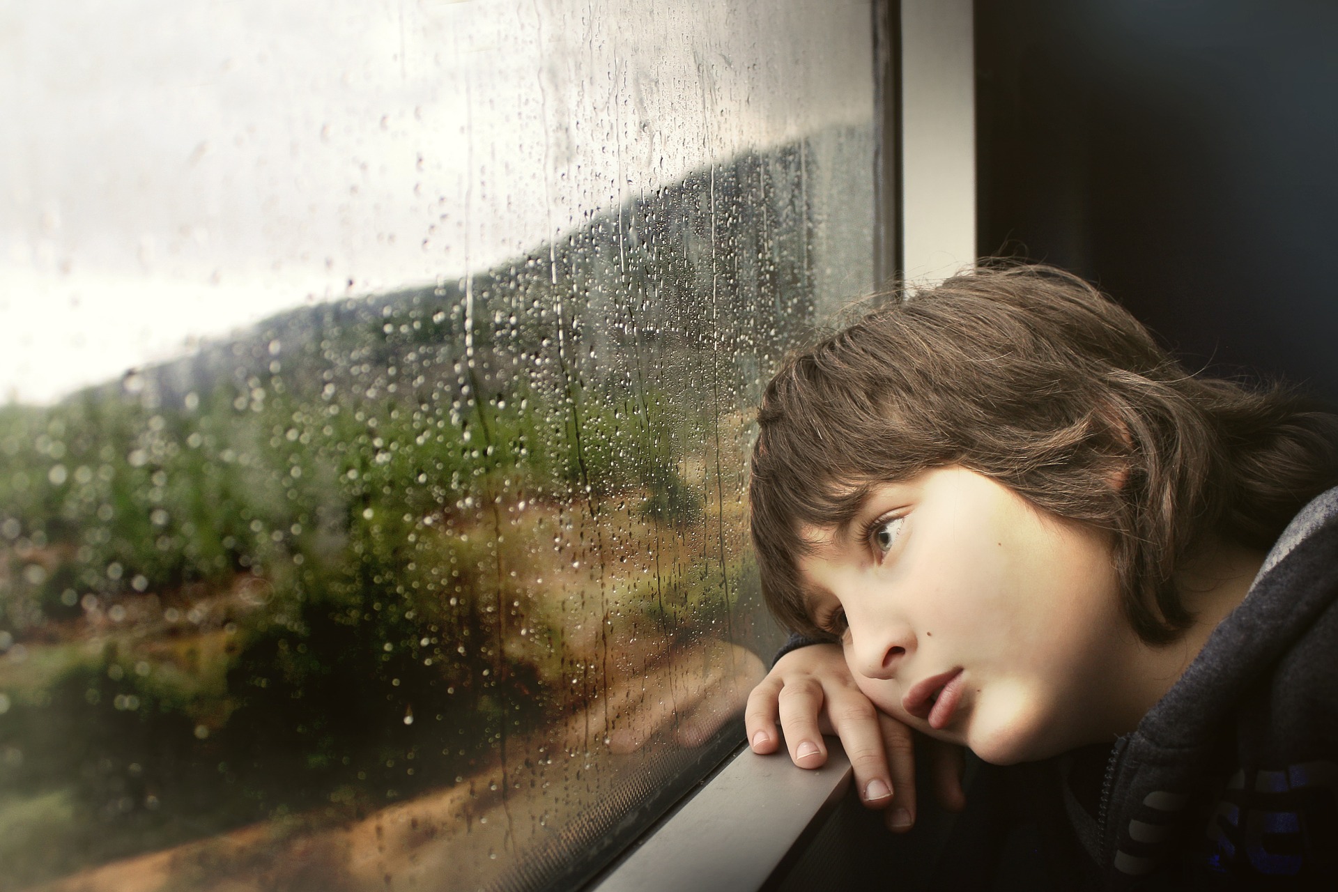 Lonely boy looking out the rainy window